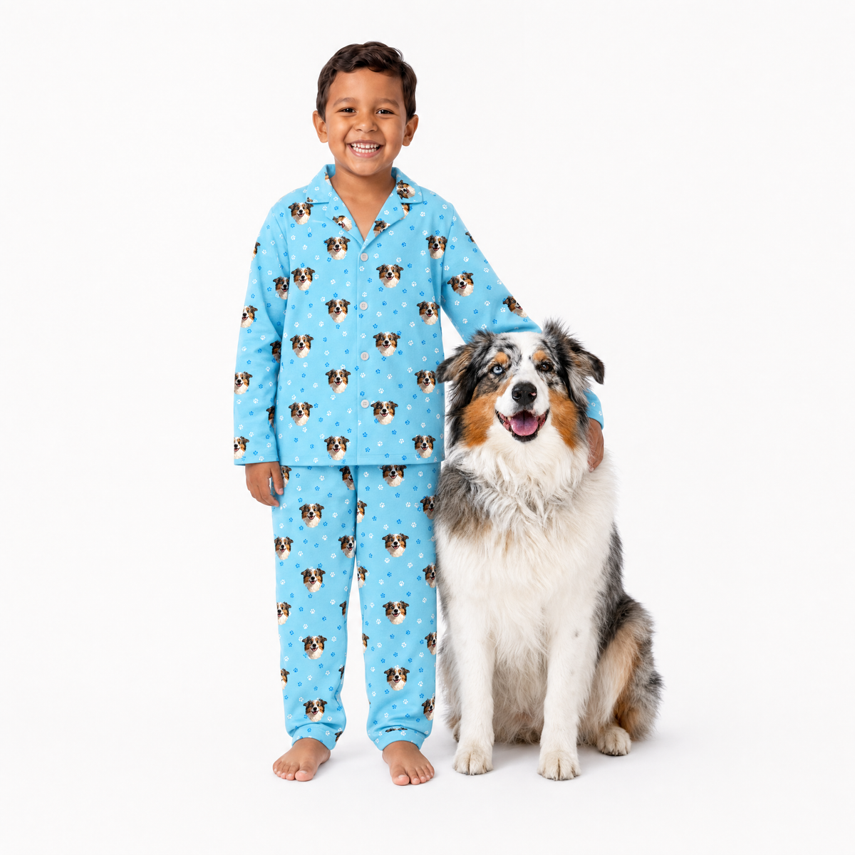 Child wearing light blue pajamas with dog pattern sitting next to a dog on a white background