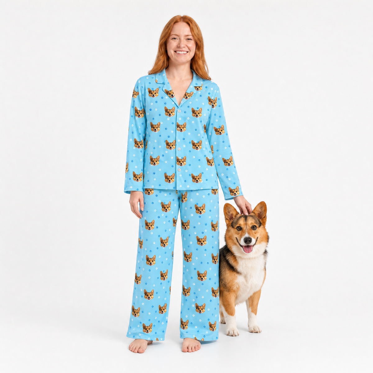 Woman wearing light blue pajamas with dog pattern standing next to a dog on a white background