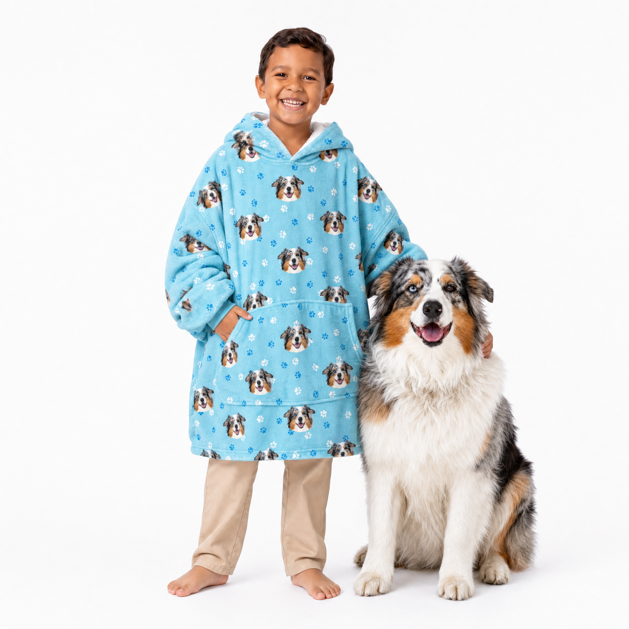 Child wearing a light blue blanket hoodie with dog pattern standing next to a dog on a white background