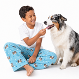 Child in pajama pants with dog pattern sitting next to a dog on a white background