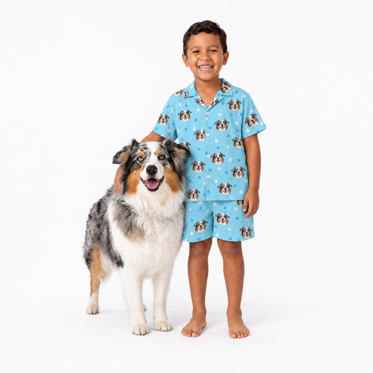 Child wearing a light blue pajama set with dog pattern standing next to a dog on a white background