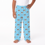 A person wearing light blue pajama pants with a repeating pattern of dog faces and small white dots, shown from the waist down against a plain white studio background.
