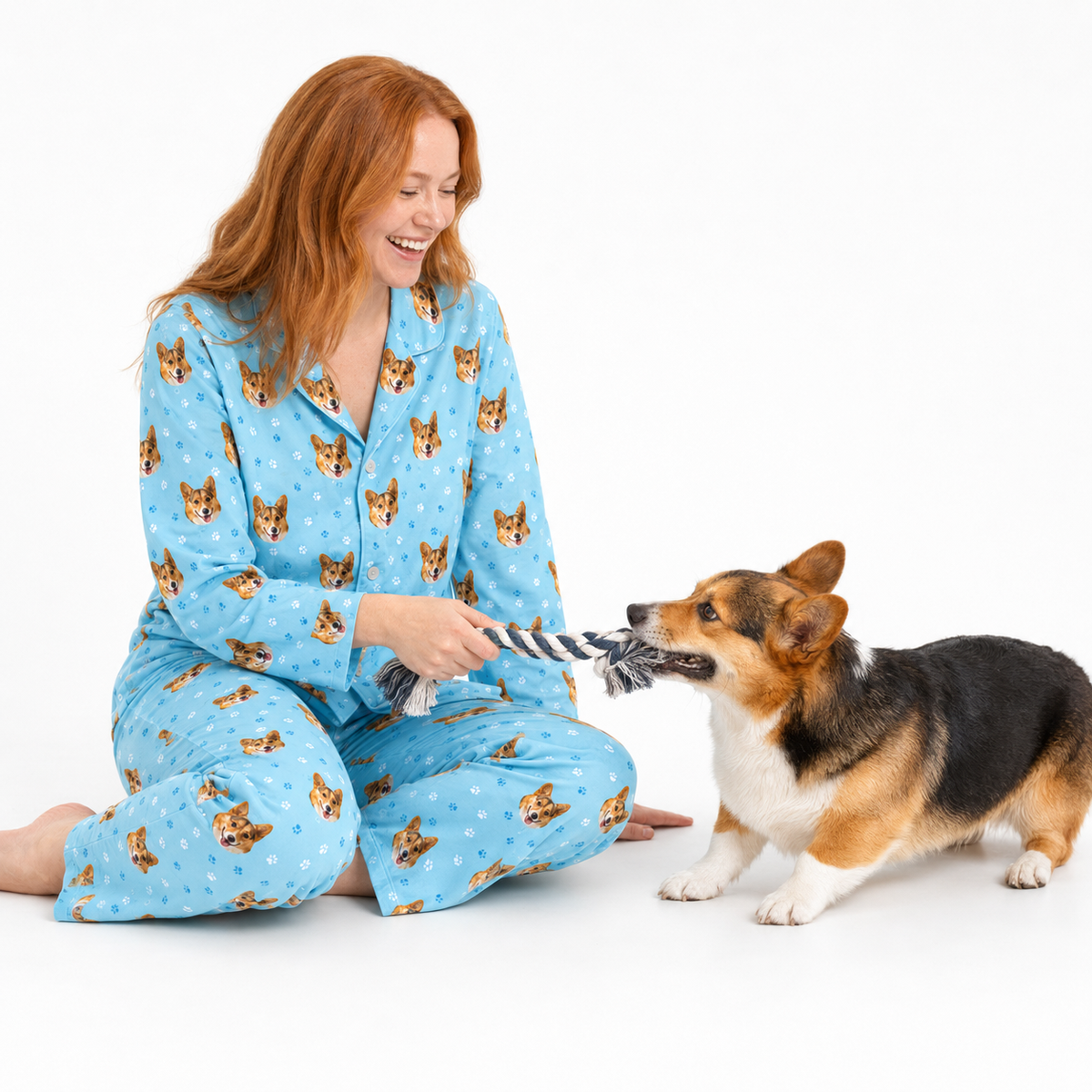 Woman in light blue paws pajamas with dog pattern sitting on the floor with a dog.