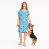Woman wearing a light blue nightgown with dog pattern holding a corgi on a white background