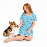 Woman wearing a light blue nightgown with dog pattern sitting next to a dog on a white background