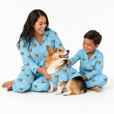 Woman, child, and corgi wearing matching light blue custom pet pajamas with a repeating dog face and paw print pattern.