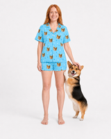 Woman wearing a light blue paws pajama set with dog pattern, standing next to a dog on a white background