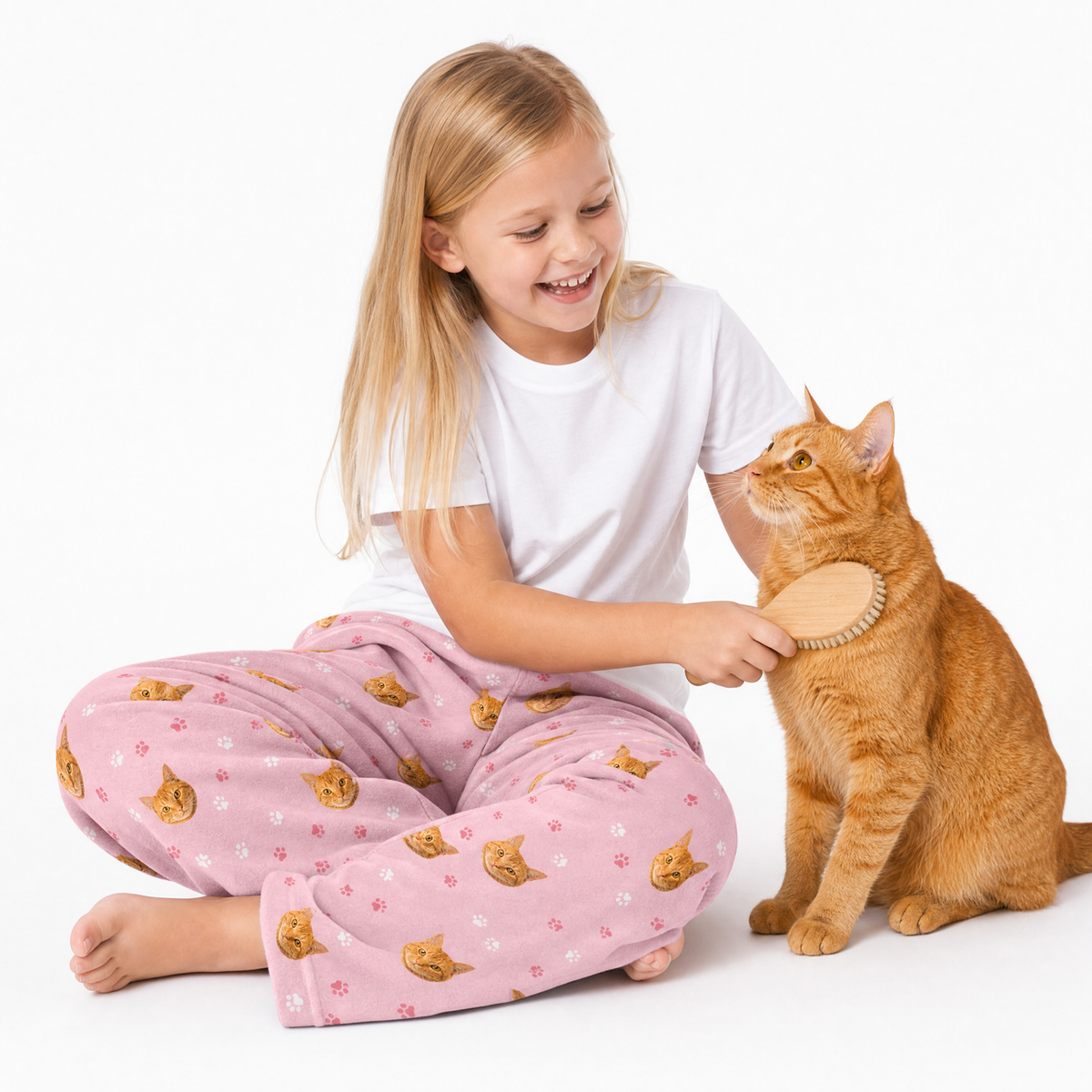 Light pink paws theme – child in cat-print pajamas brushing orange cat.