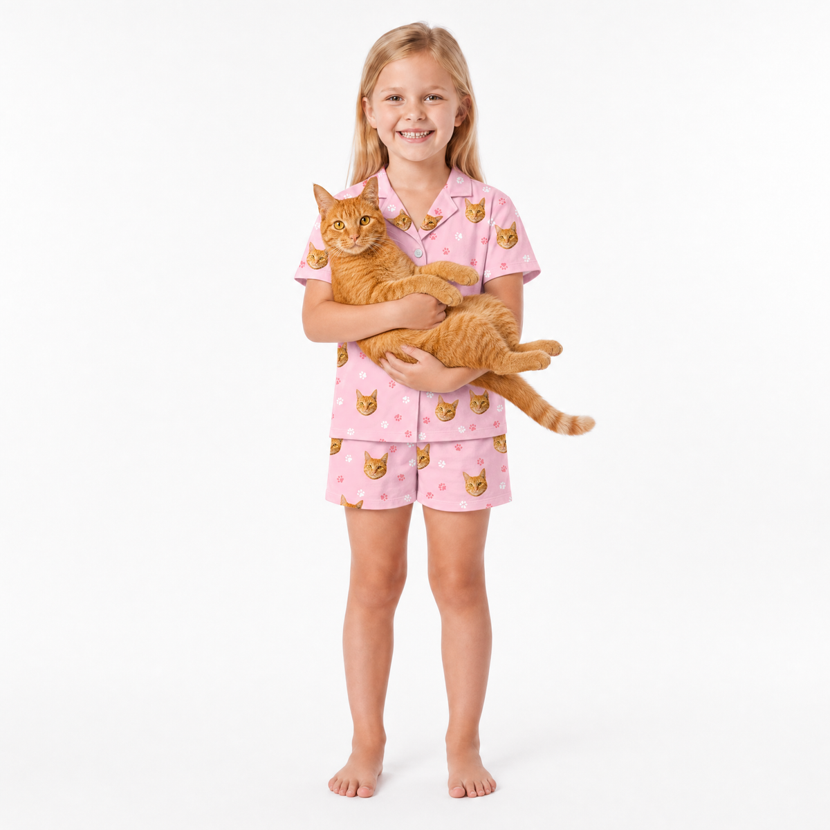 Girl wearing pink pajamas with cat patterns, holding an orange cat on a white background