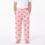 Light Pink children's pajama pants with an all-over print of orange tabby cat faces and small pink hearts, shown on a child wearing a white t-shirt against a plain white background.