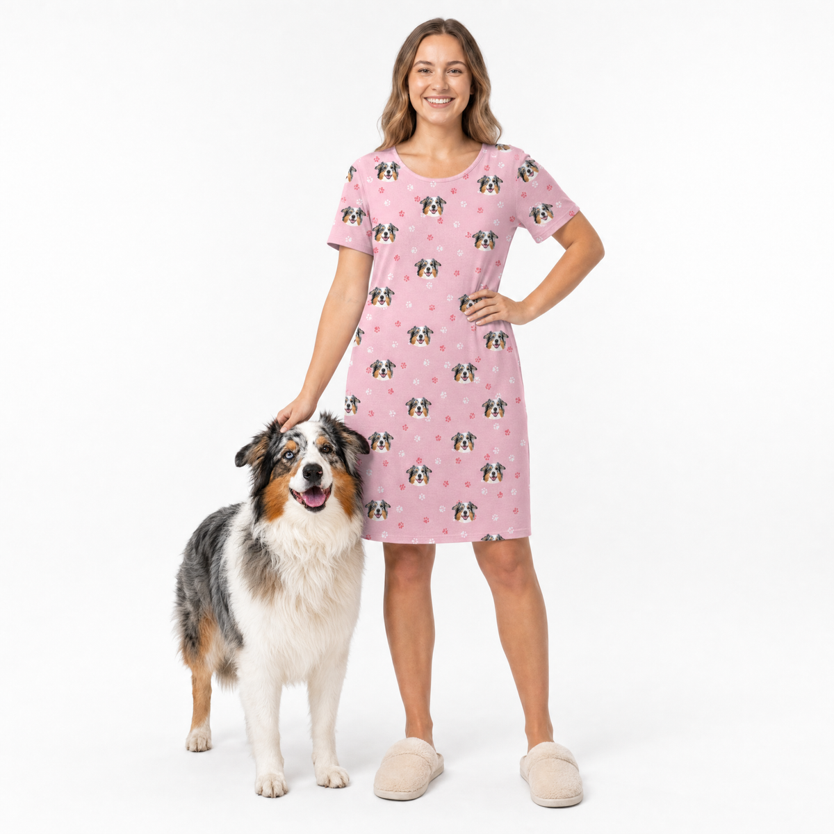 Woman wearing a pink dog patterned nightgown standing next to a dog on a white background