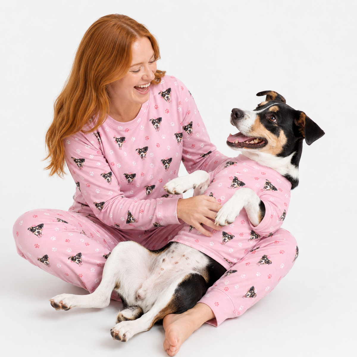 Woman and dog wearing matching light pink custom pet pajamas with a repeating dog face and paw print pattern.