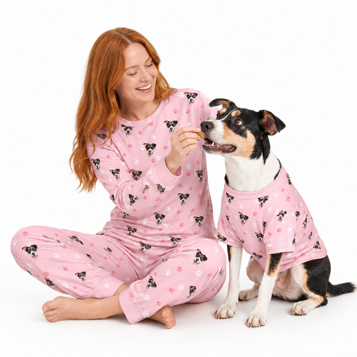 Woman and dog wearing matching light pink custom pet pajamas with a repeating dog face and paw print pattern.