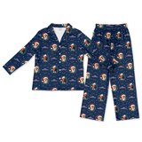 A two-piece children's pajama set featuring a long-sleeve button-up top and matching pants, both in navy blue with an all-over Christmas dog print. The print includes dogs wearing Santa hats, snowflakes, and purple holiday text on a white background.