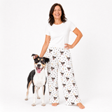 Woman wearing a white t-shirt and patterned pajama pants with a dog standing next to her on a white background