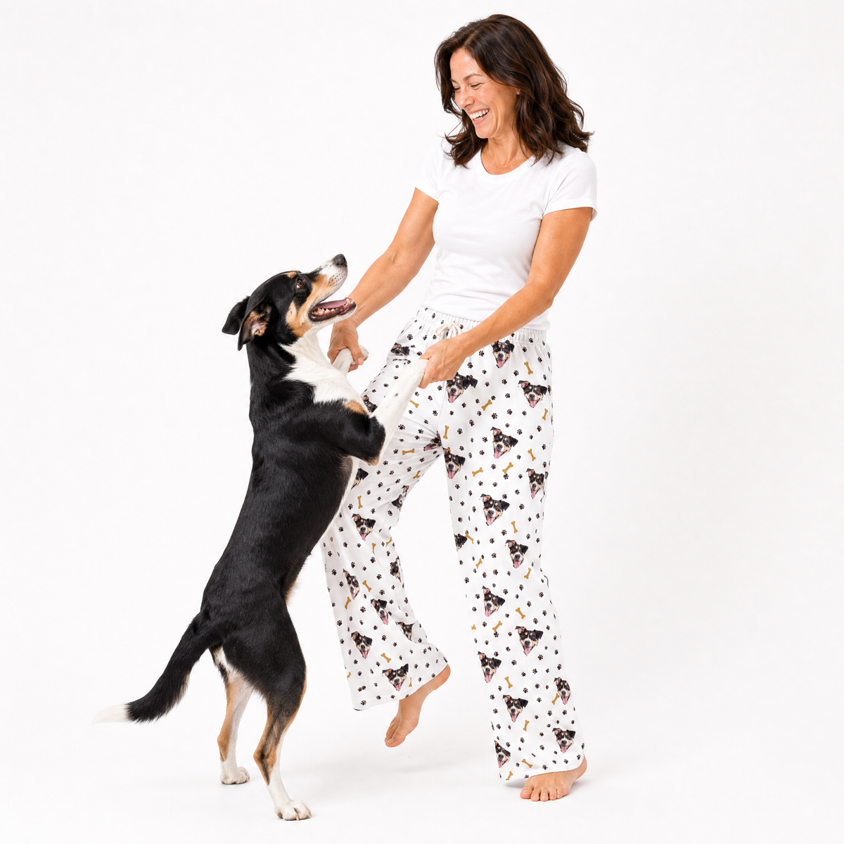 Woman wearing patterned pajama pants standing next to a dog on a white background
