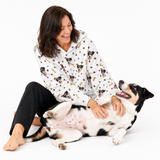 Woman wearing a white patterned blanket hoodie sitting with a large dog on a white background