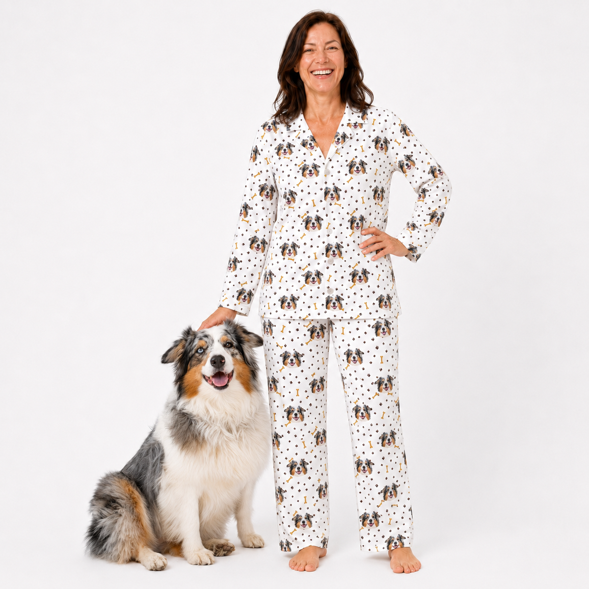 Woman wearing a pajama set with dog pattern standing next to a dog on a white background