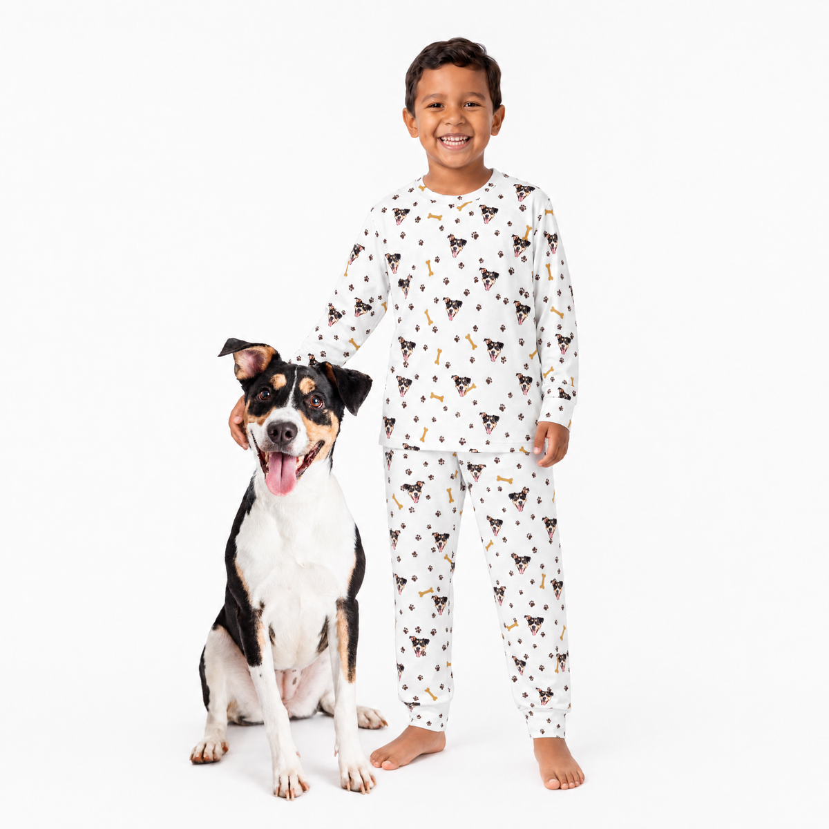 Child wearing a white jogger pajama set with dog pattern standing next to a dog on a white background