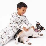 Child in white jogger pajamas playing with a dog on a white background