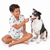 Child in white pajamas with dog and bone prints sitting next to a dog on a white background