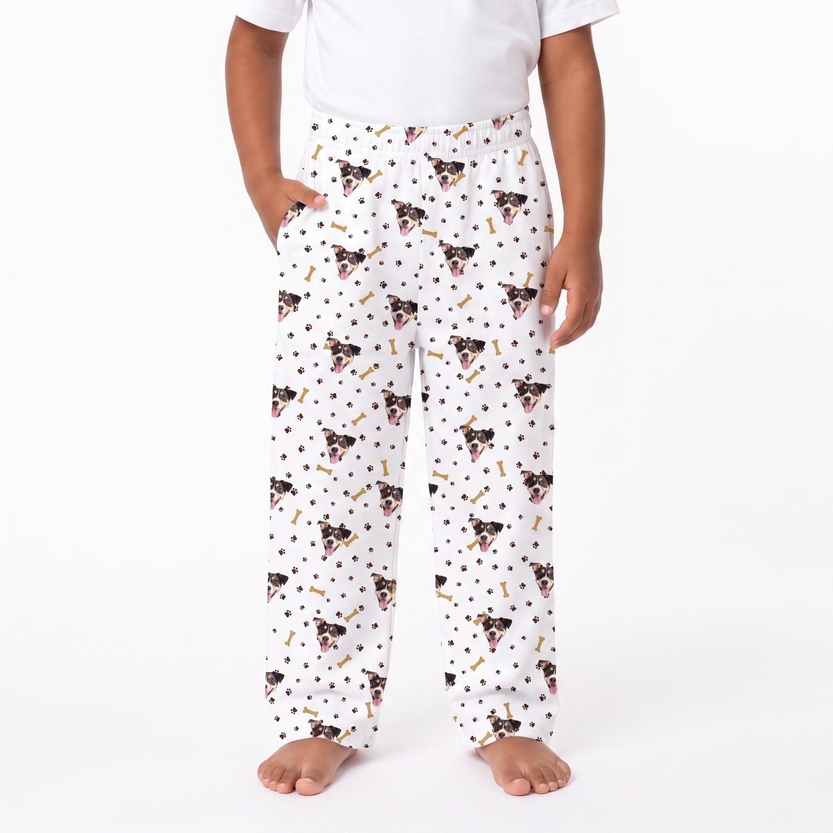paw and bones pajama pants with an all-over print of Boston Terrier dog faces, black polka dots, and small gold bones, modeled on a child against a white background.