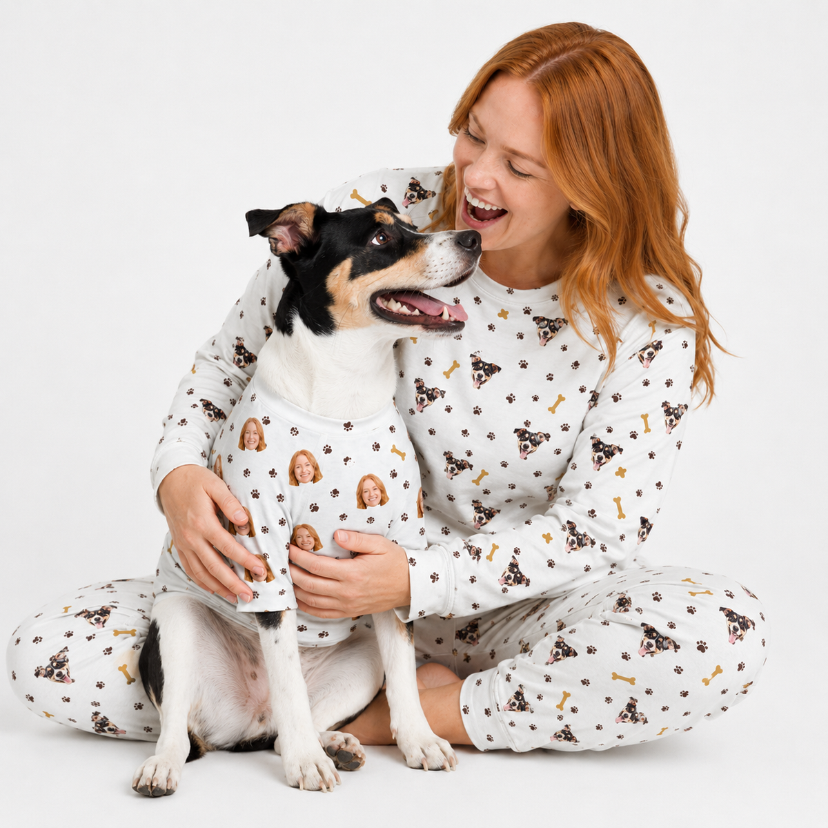 Woman and dog wearing matching white custom pet pajamas with a repeating dog face, paw print, and bone pattern.