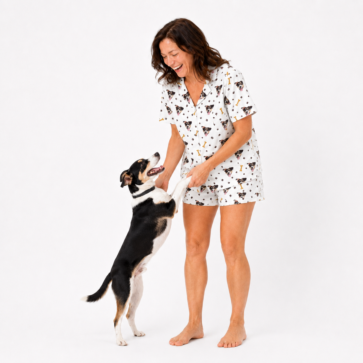 Woman in a matching dog-themed pajama set standing next to a dog on a white background