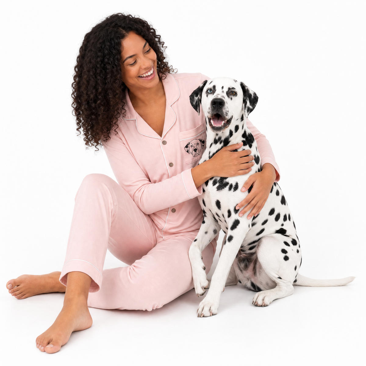 Woman in pink pajamas sitting with a Dalmatian dog on a white background