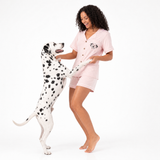 Woman in pink pajama set standing next to a Dalmatian dog on a white background