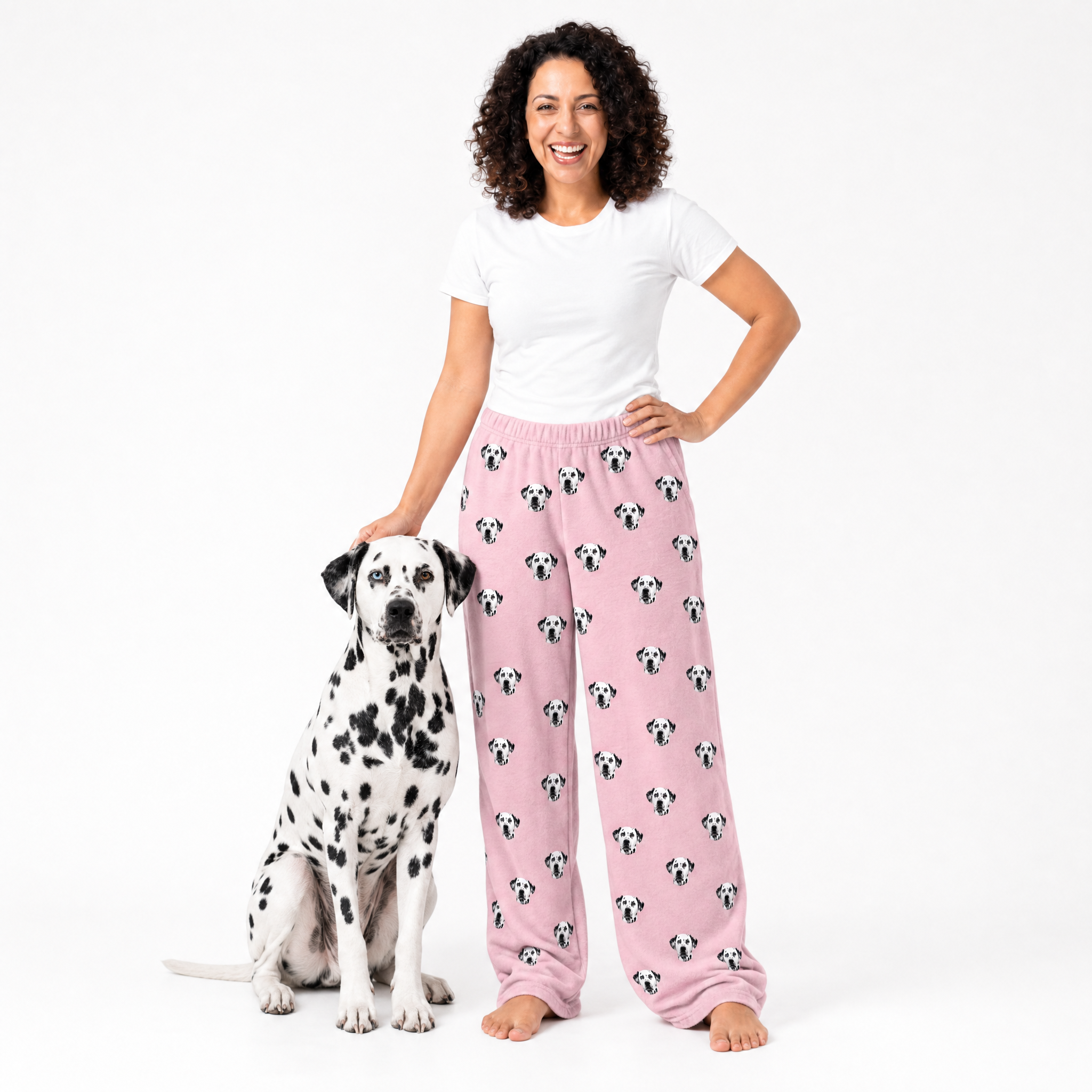 Woman wearing pink pajama pants with dog pattern standing next to a Dalmatian dog on a white background