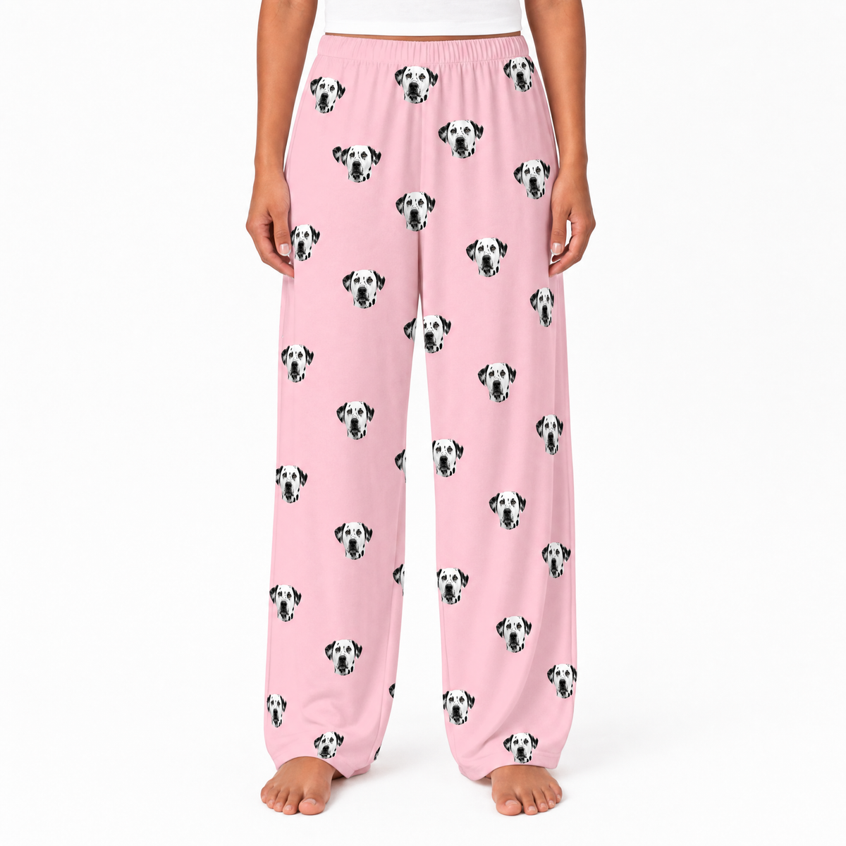Pink pajama pants with dalmatian dog pattern worn by a person on a white background
