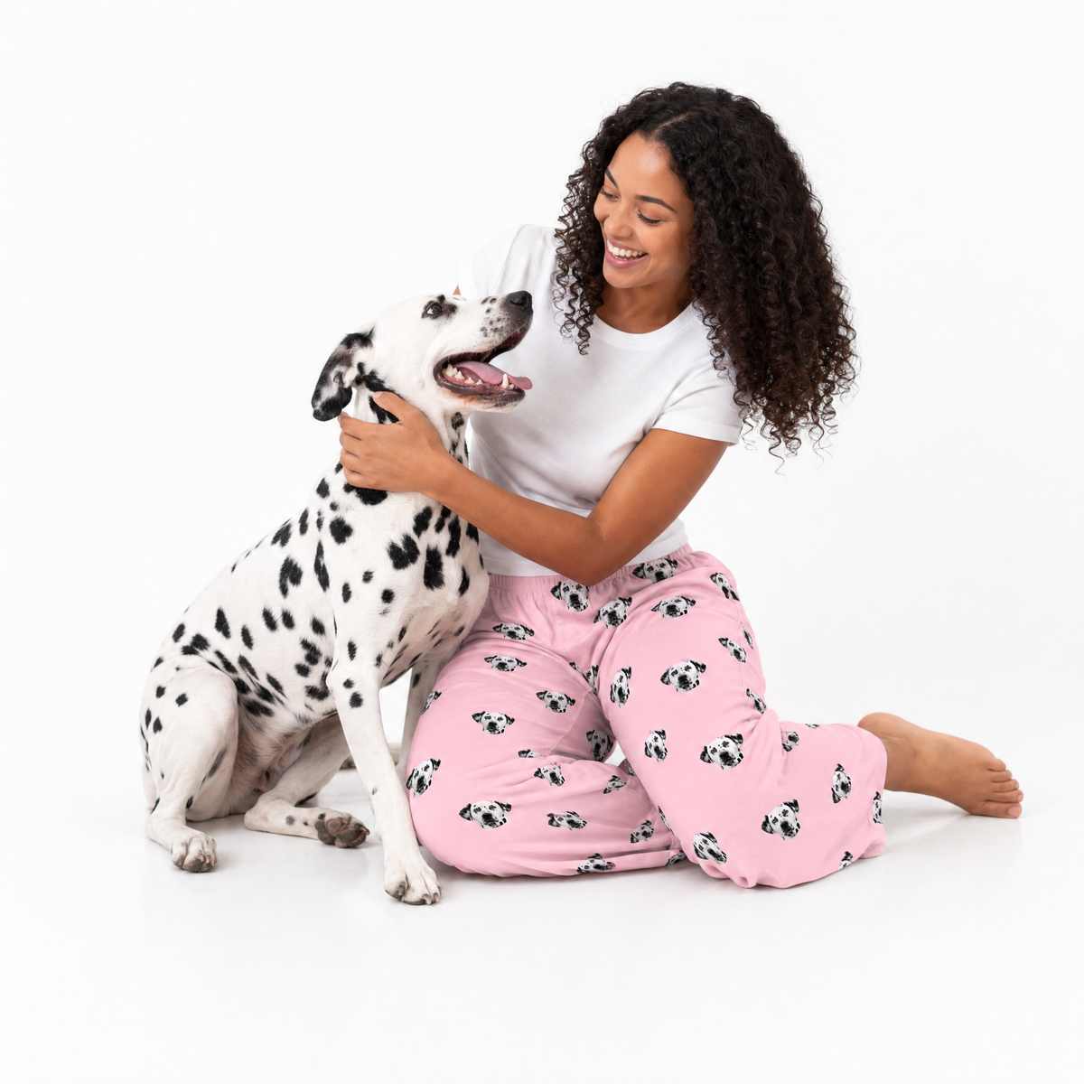 Woman in pink pajama pants with dog pattern sitting on the floor with a Dalmatian dog.