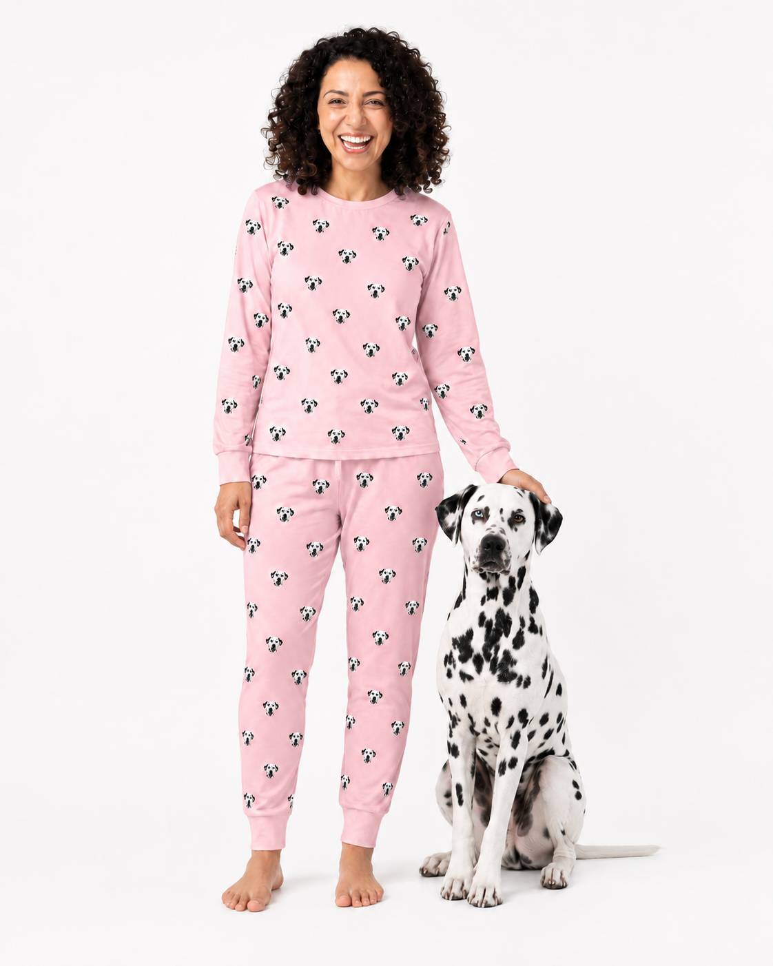 Woman wearing pink jogger pajamas with dog pattern sitting next to a Dalmatian dog on a white background