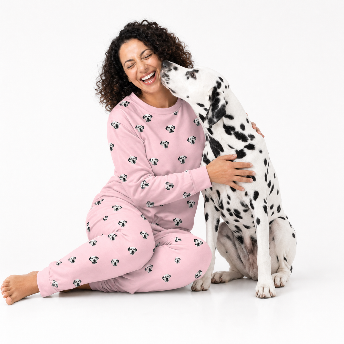 Woman wearing a Pink Dream Dalmatian-print pajama set sitting on the floor while a Dalmatian licks her cheek.