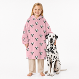 Child wearing a pink blanket hoodie with Dalmatian pattern standing next to a Dalmatian dog on a white background