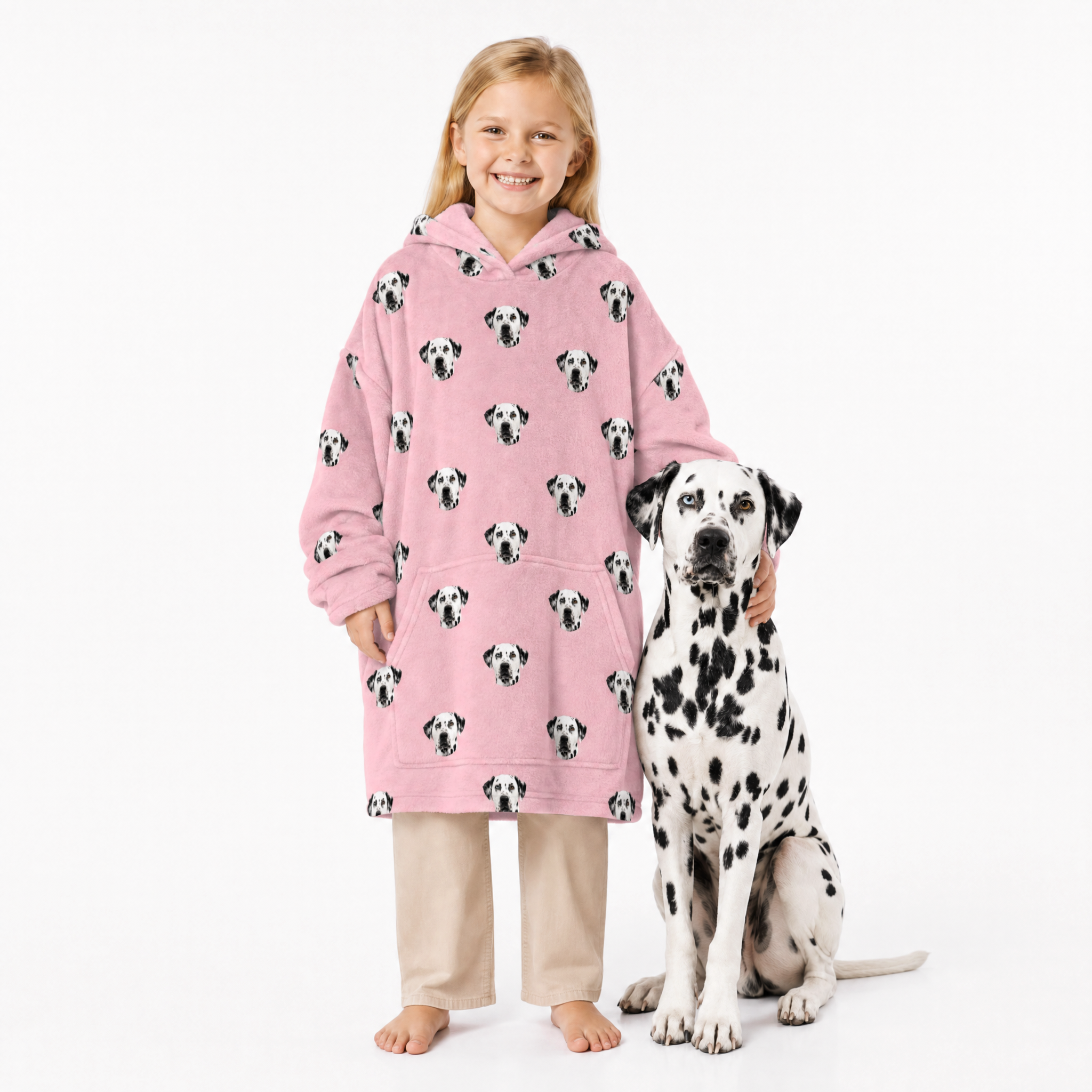 Child wearing a pink blanket hoodie with Dalmatian pattern standing next to a Dalmatian dog on a white background