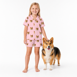 Girl wearing pink pajamas with dog pattern standing next to a dog on a white background
