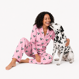 Woman wearing a Pink Dream Dalmatian-print pajama set sitting beside a Dalmatian that is licking her cheek.