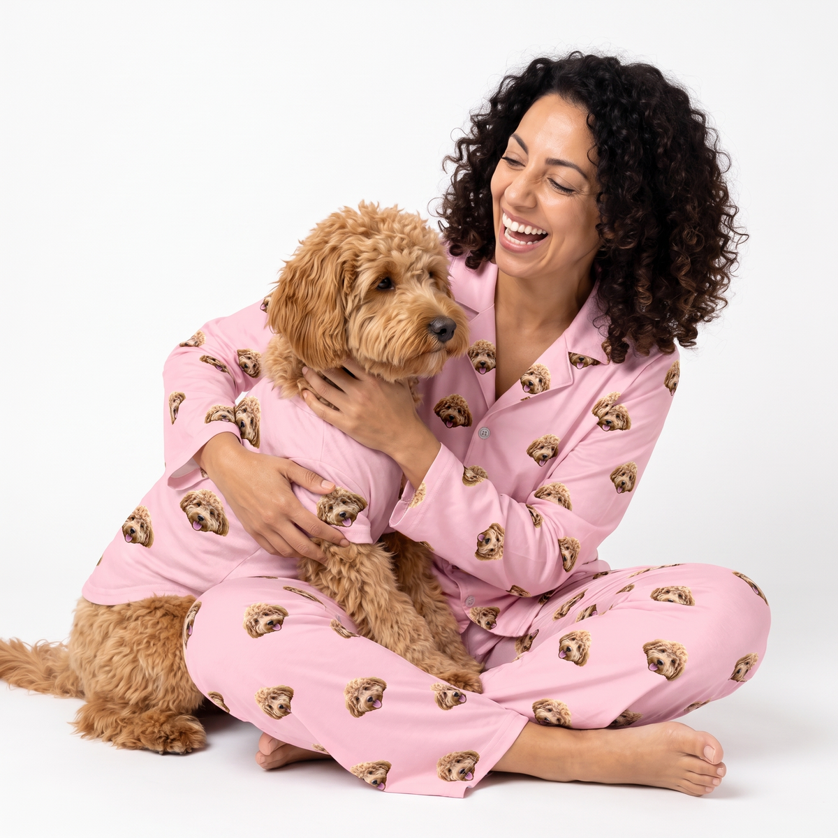 Woman and poodle mix wearing matching pink custom pet pajamas with a repeating dog face pattern.