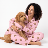 Woman and poodle mix wearing matching pink custom pet pajamas with a repeating dog face pattern.