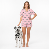 Woman wearing pink pajama set with dog pattern, standing next to a dalmatian dog on a white background