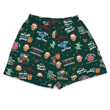 A pair of dark green Christmas-themed boxer shorts featuring a repeating pattern of a greyhound dog's face wearing a Santa hat, holiday quotes, and festive illustrations, shown against a plain white background.