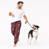 Man wearing plaid pajama pants with a dog on a leash against a white background