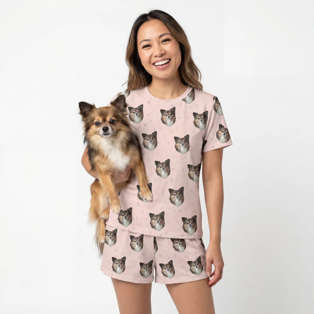 Woman wearing a pink pajama set with dog patterns, holding a small dog. [BlushBlossoms]