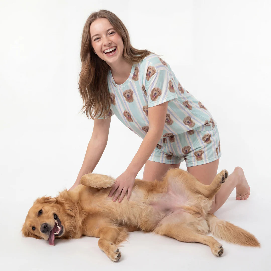 Woman in patterned pajamas playing with a golden retriever on a white background