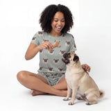 Woman in pug-themed pajamas holding a bone-shaped toy with a pug sitting next to her on a white background