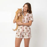 Woman wearing a pajama set with cat designs, holding an orange cat against a white background
