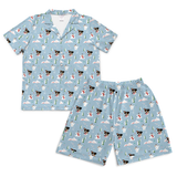 A two-piece short-sleeve pajama set featuring a light blue shirt and matching shorts with an all-over print of Boston Terrier dogs, white cats, and snowmen on a snowy background.