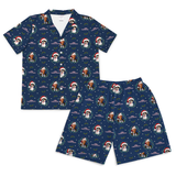 A two-piece pajama set featuring a short-sleeve button-up shirt and matching shorts in a green plaid pattern with Dalmatian dog faces, pink figures, and small colorful patches, shown on a plain white background.